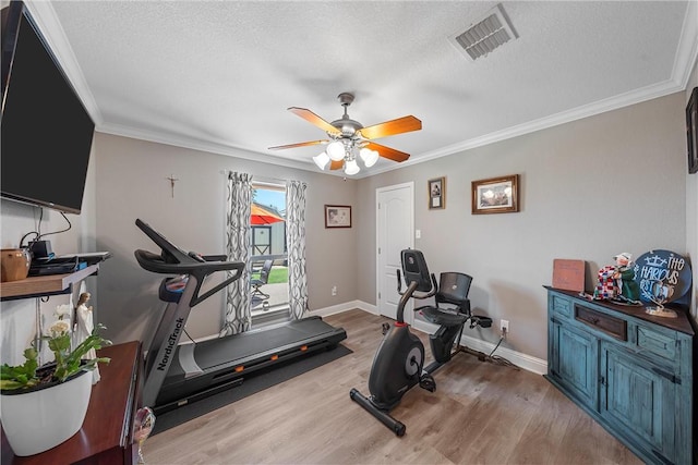 exercise area with light wood-type flooring, ornamental molding, and a textured ceiling