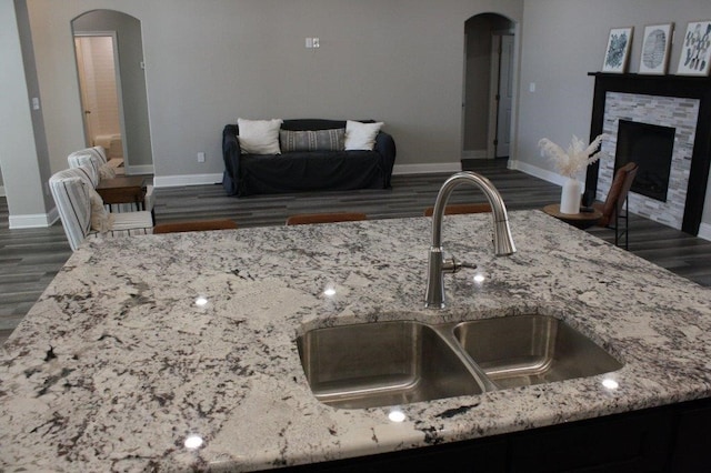 kitchen featuring a fireplace, light stone counters, sink, and dark wood-type flooring