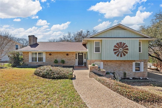 split level home with brick siding, a chimney, and a front lawn