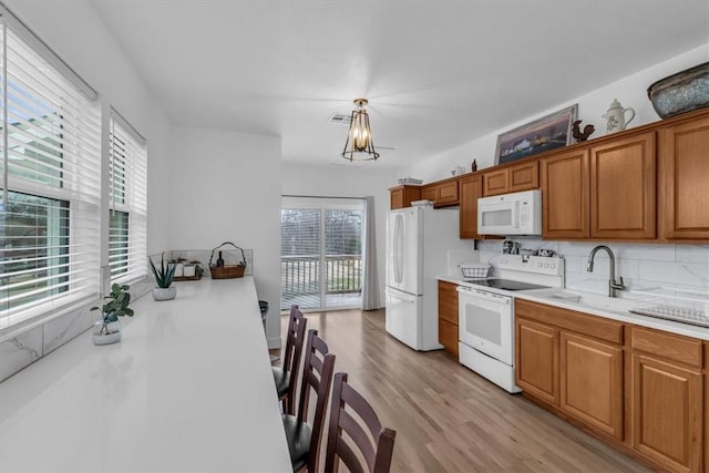 kitchen with white appliances, decorative light fixtures, light hardwood / wood-style flooring, and tasteful backsplash