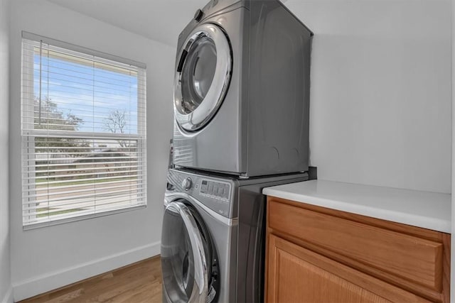 laundry area with stacked washer and dryer, cabinets, and light wood-type flooring