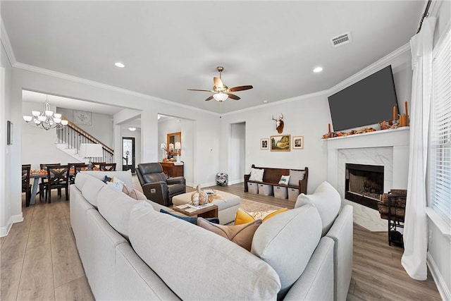 living room with ceiling fan with notable chandelier, light wood-type flooring, crown molding, and a premium fireplace