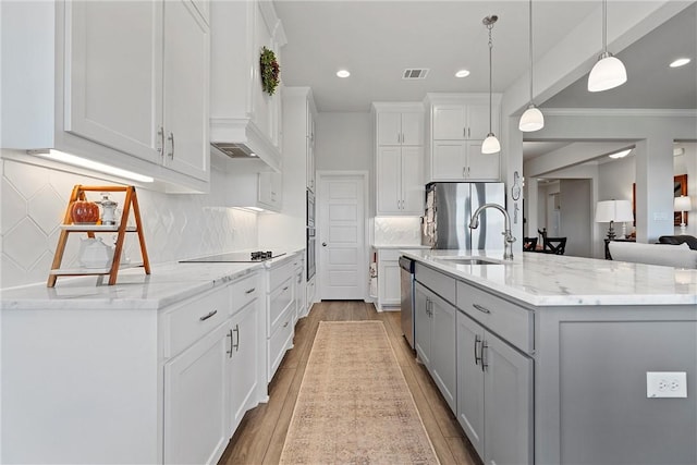 kitchen with appliances with stainless steel finishes, light wood-type flooring, a large island with sink, pendant lighting, and white cabinetry