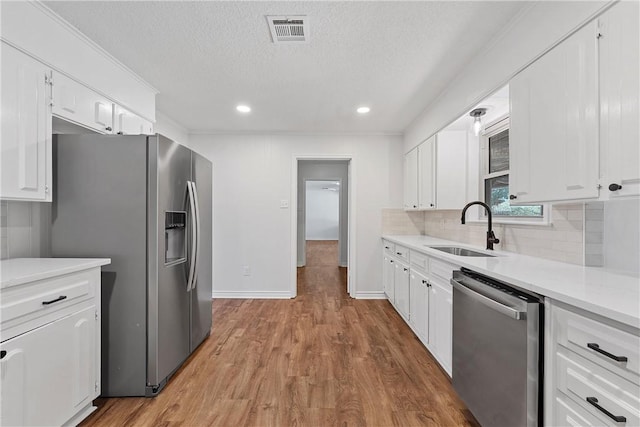 kitchen with sink, tasteful backsplash, light wood-type flooring, stainless steel appliances, and white cabinets