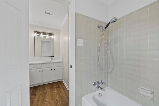 bathroom with tiled shower / bath, hardwood / wood-style floors, vanity, crown molding, and a textured ceiling