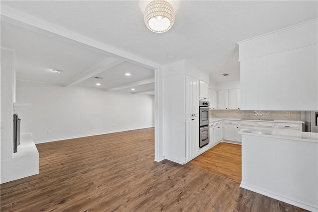 kitchen with white cabinetry, beam ceiling, tasteful backsplash, wood-type flooring, and stainless steel double oven