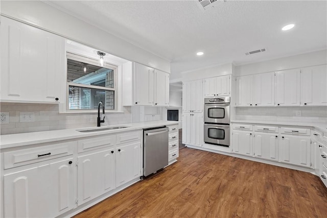 kitchen featuring sink, white cabinetry, appliances with stainless steel finishes, hardwood / wood-style floors, and backsplash