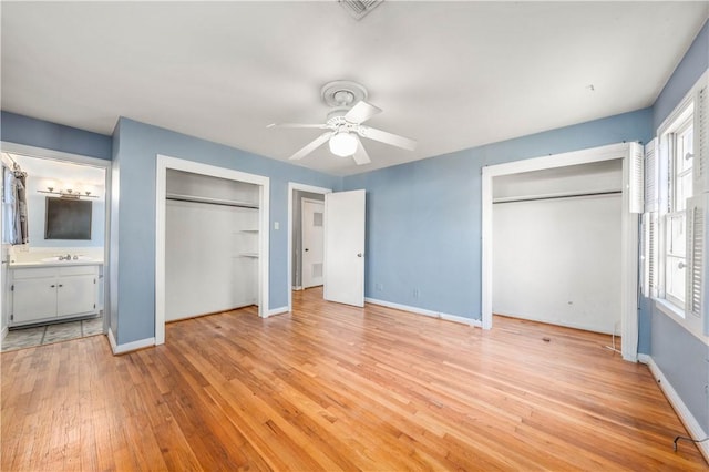 unfurnished bedroom with ceiling fan, multiple closets, connected bathroom, and light hardwood / wood-style flooring