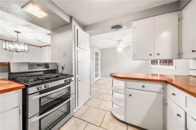 kitchen featuring pendant lighting, stainless steel gas range oven, wooden counters, ceiling fan with notable chandelier, and white cabinetry