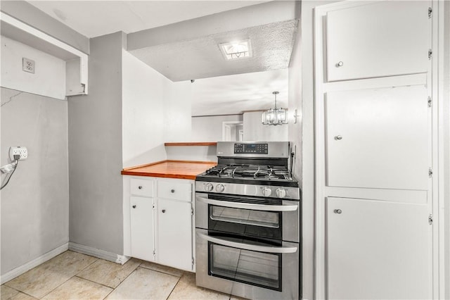 kitchen featuring wood counters, light tile patterned floors, white cabinets, hanging light fixtures, and stainless steel range with gas stovetop