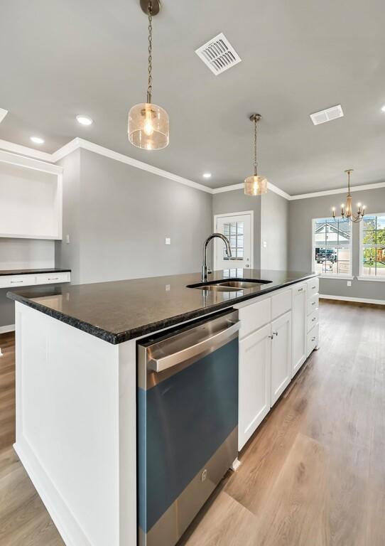 kitchen featuring decorative light fixtures, a center island with sink, stainless steel dishwasher, and sink