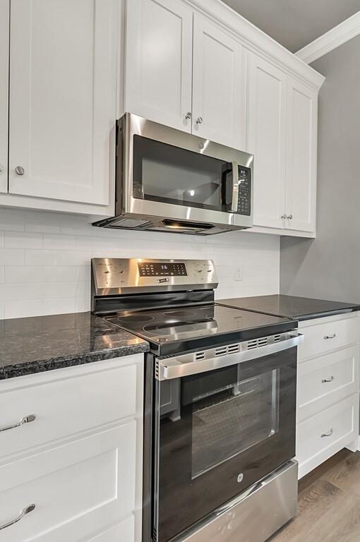 kitchen featuring white cabinetry, dark hardwood / wood-style flooring, crown molding, dark stone counters, and appliances with stainless steel finishes