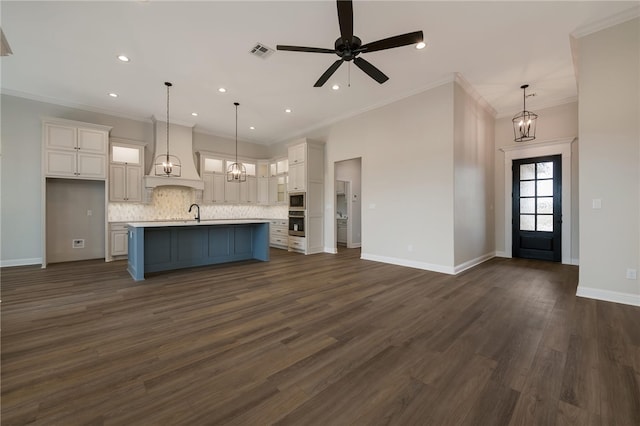 kitchen with decorative light fixtures, a center island with sink, dark hardwood / wood-style floors, and ornamental molding