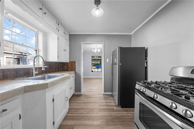 kitchen with sink, white cabinets, ornamental molding, stainless steel appliances, and light hardwood / wood-style flooring