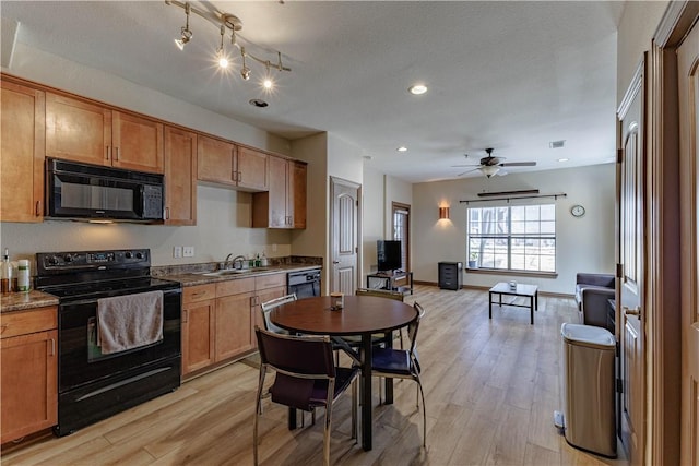 kitchen featuring baseboards, a sink, black appliances, light wood-style floors, and dark countertops