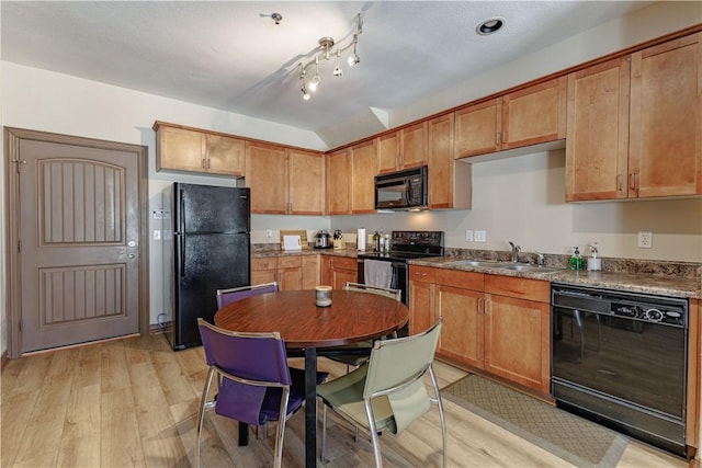 kitchen with a sink, black appliances, brown cabinetry, and light wood finished floors