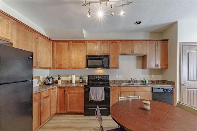 kitchen with light wood-type flooring, black appliances, a sink, dark stone countertops, and a textured ceiling