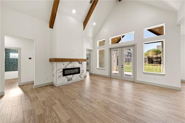 unfurnished living room featuring beam ceiling, french doors, a high end fireplace, high vaulted ceiling, and light hardwood / wood-style floors