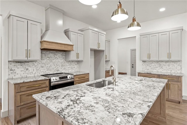 kitchen featuring stainless steel electric range, custom range hood, sink, and a kitchen island with sink