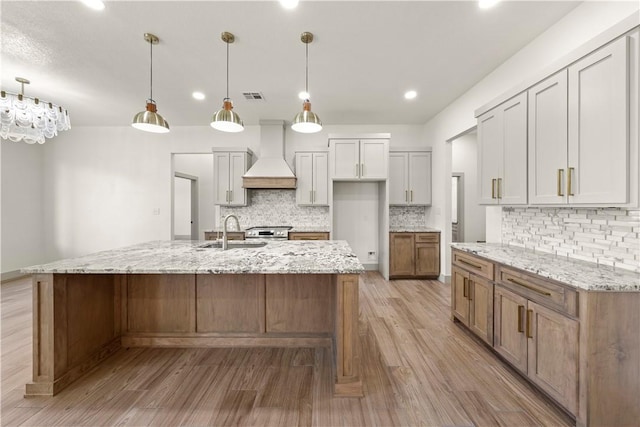 kitchen featuring pendant lighting, premium range hood, a large island with sink, and light hardwood / wood-style flooring