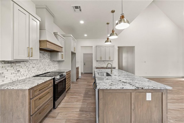 kitchen featuring stainless steel electric range oven, sink, light stone countertops, decorative light fixtures, and custom exhaust hood