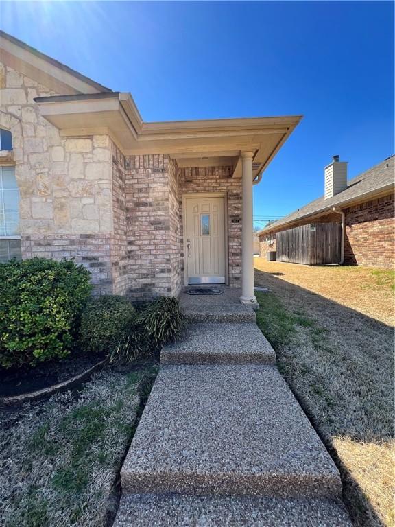 view of exterior entry featuring fence and brick siding