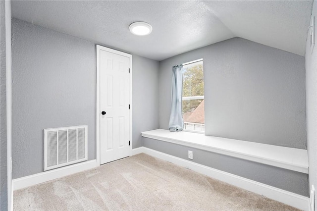 interior space with a textured ceiling, light colored carpet, and vaulted ceiling