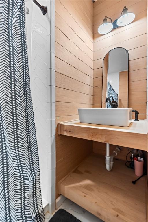 bathroom featuring a tile shower, wood walls, and vanity