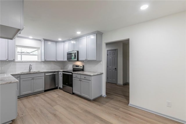 kitchen with light stone countertops, light hardwood / wood-style floors, stainless steel appliances, sink, and gray cabinets