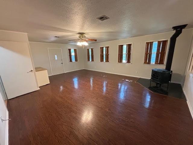 unfurnished living room with ceiling fan, dark hardwood / wood-style flooring, a wood stove, and a textured ceiling