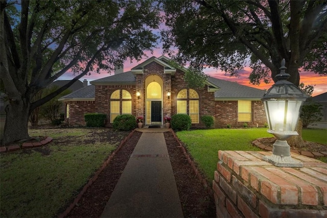 view of front of house featuring brick siding and a lawn