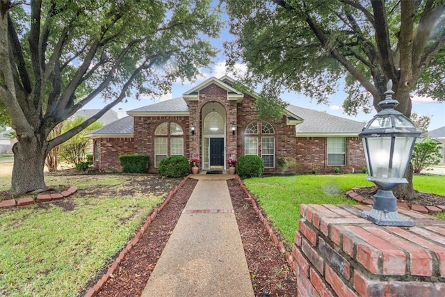 traditional home with roof with shingles, a front lawn, and brick siding