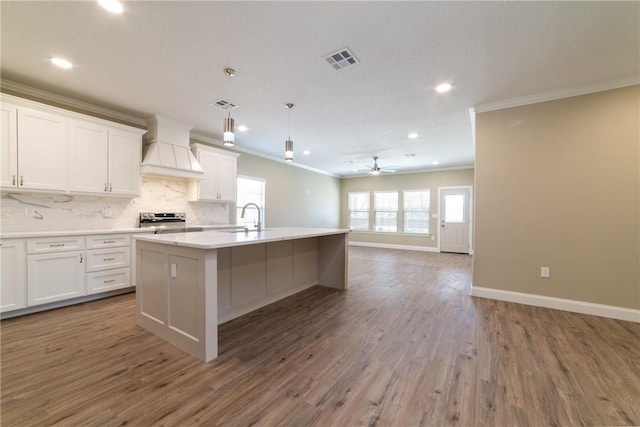 kitchen featuring ornamental molding, custom exhaust hood, hardwood / wood-style floors, white cabinetry, and an island with sink