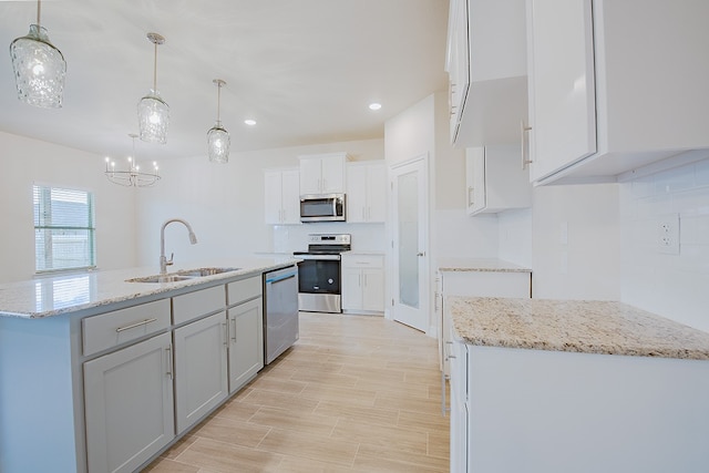 kitchen with stainless steel appliances, a kitchen island with sink, sink, white cabinetry, and hanging light fixtures