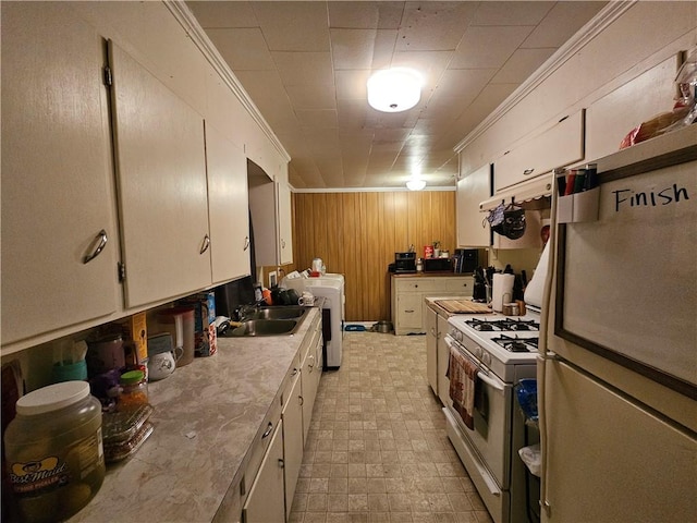 kitchen with wood walls, washer / dryer, sink, ornamental molding, and white appliances