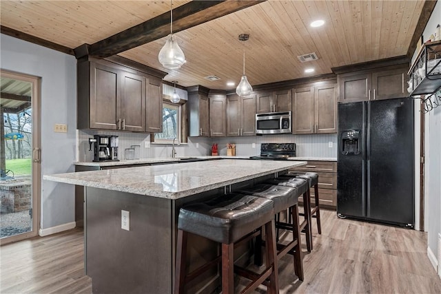 kitchen with dark brown cabinetry, light stone counters, pendant lighting, decorative backsplash, and black appliances