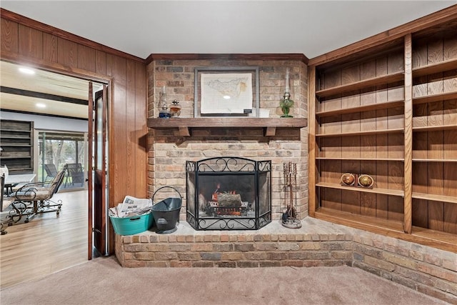 carpeted living room featuring built in features, wooden walls, and a brick fireplace