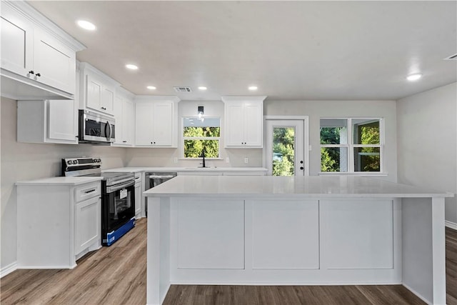 kitchen with white cabinets, sink, light hardwood / wood-style flooring, appliances with stainless steel finishes, and a kitchen island