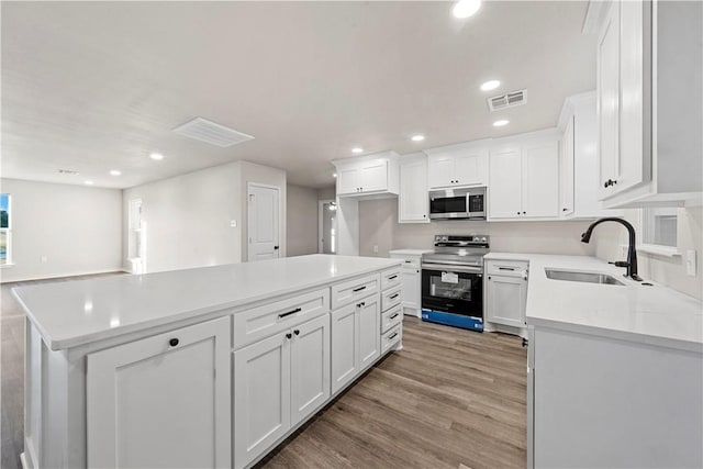 kitchen with stainless steel appliances, sink, white cabinets, light hardwood / wood-style floors, and a kitchen island