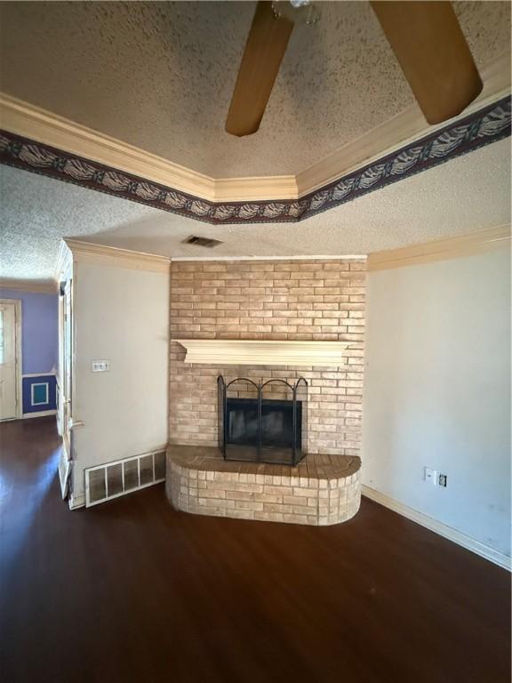 unfurnished living room with a textured ceiling, dark hardwood / wood-style floors, crown molding, and a brick fireplace