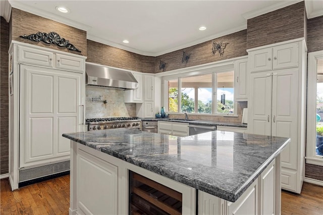 kitchen with hardwood / wood-style floors, dark stone countertops, wall chimney range hood, and appliances with stainless steel finishes