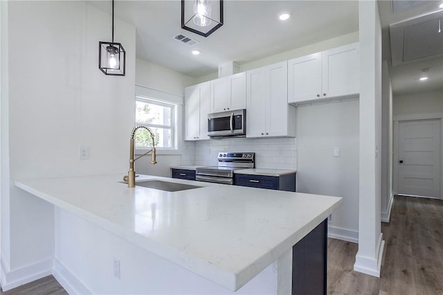 kitchen with kitchen peninsula, white cabinets, pendant lighting, and appliances with stainless steel finishes