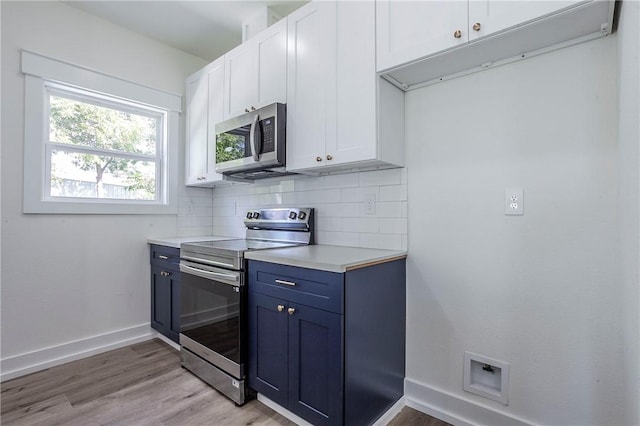 kitchen with backsplash, white cabinets, blue cabinets, light wood-type flooring, and appliances with stainless steel finishes