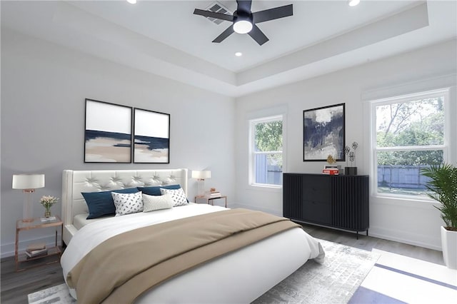 bedroom with a tray ceiling, multiple windows, ceiling fan, and hardwood / wood-style floors