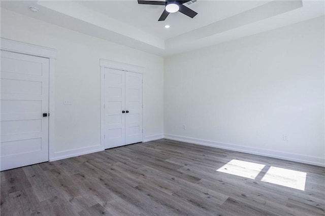 unfurnished bedroom featuring hardwood / wood-style floors, a raised ceiling, and ceiling fan