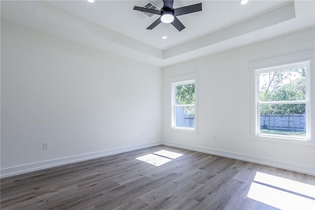 unfurnished room with hardwood / wood-style flooring, a raised ceiling, ceiling fan, and a healthy amount of sunlight