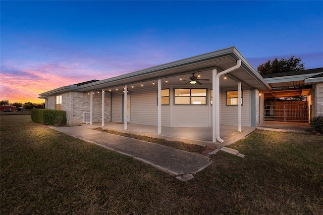 back house at dusk with a lawn, ceiling fan, and a porch