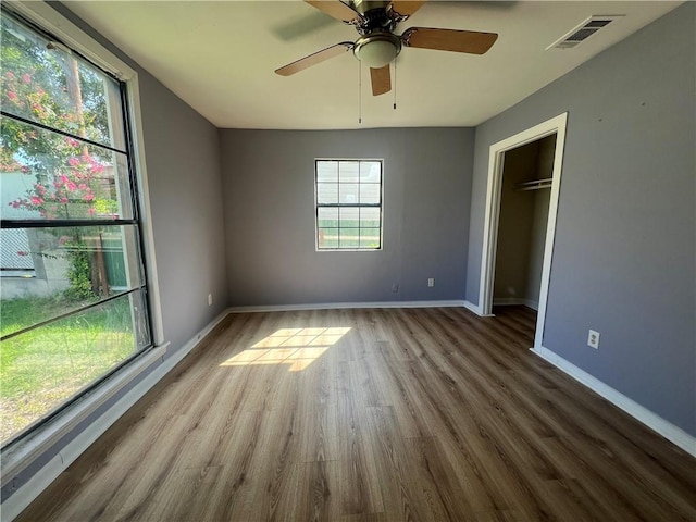 unfurnished bedroom with wood-type flooring, a closet, a spacious closet, and ceiling fan