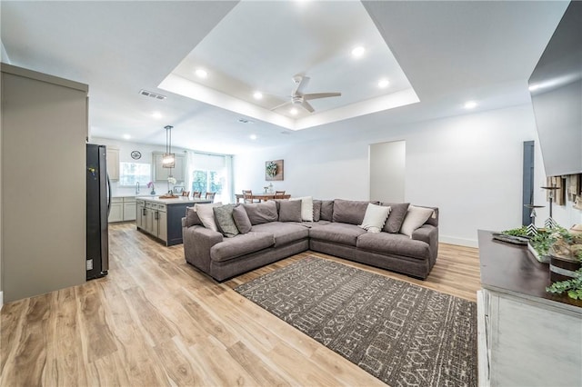 living room featuring ceiling fan, light hardwood / wood-style floors, and a tray ceiling