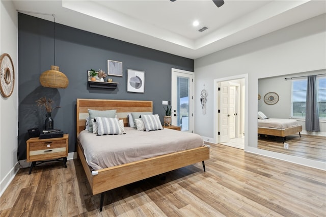 bedroom featuring baseboards, a tray ceiling, visible vents, and wood finished floors